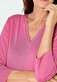 Rosa Langarmshirt mit V-Ausschnitt und gewellten Abschlüssen, aus weichem Stoff mit leicht strukturierten Oberflächen und lockeren Ärmeln.