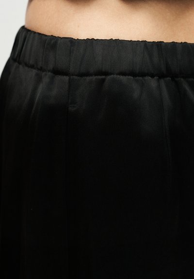 Κοντινό πλάνο στη μέση ατόμου που φοράει μαύρο παντελόνι με ελαστική μέση από απαλό, ελαφρώς γυαλιστερό ύφασμα.