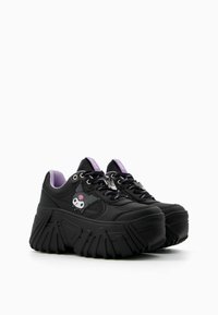Black platform sneakers with a chunky rubber sole, purple accents, and a cartoon skull design on the side. Features black laces.