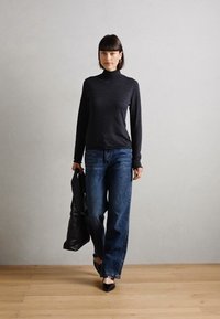 Svart høyhalset genser, avslappede blå denim vid bukser, og svart lærveske; modell i svarte leiligheter, stående på tregulv.