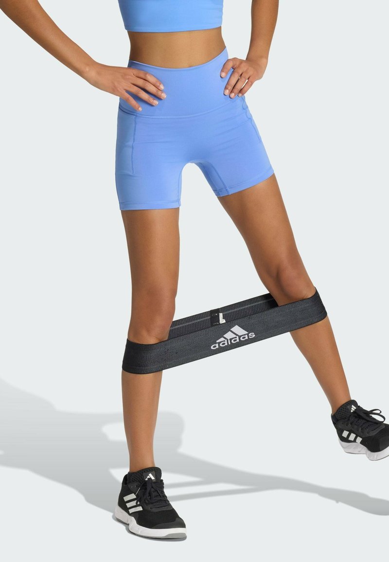 Bande de résistance noire avec le logo « adidas » autour des cuisses, portée avec un short bleu clair. Chaussures de sport noires avec des accents blancs. Environnement de fitness.