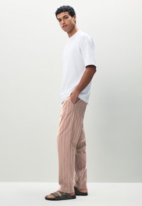 Hvid t-shirt med korte ærmer, løstsiddende lyserøde bukser med striber, og mørkegrønne slip-on sandaler med tekstureret sål.