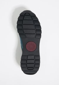 Podeszwa buta z czarnej gumy z głębokim bieżnikiem; na środku znajduje się bordowe okrągłe logo. Górna część w kolorze zielonkawoniebieskim o miękkiej teksturze.