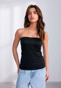 Sort skulderløs top af glat stof, tætsiddende design med lige halsudskæring, kombineret med lyseblå løstsiddende denimjeans.