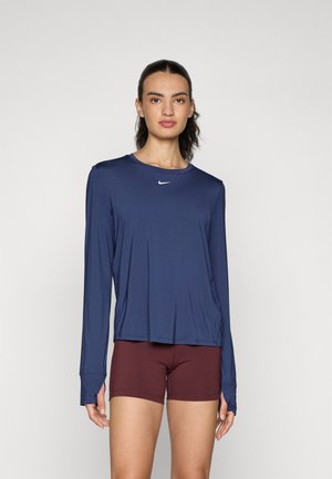 Marineblauw sportieve lange mouwen top van lichtgewicht stof, met een ronde hals en duimopening in de mouwen. Gecombineerd met strakke bordeauxrode shorts.