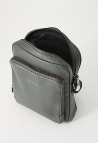Zaino in pelle grigia con molteplici scomparti con zip, superficie liscia e logo di marca. Interno visibile, con rivestimento in tessuto.