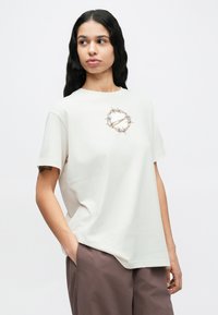 Krémové tričko s krátkym rukávom s kruhovou grafikou obsahujúcou dizajn s ostnatým drôtom a logom Swoosh, vyrobené z mäkkej bavlny.