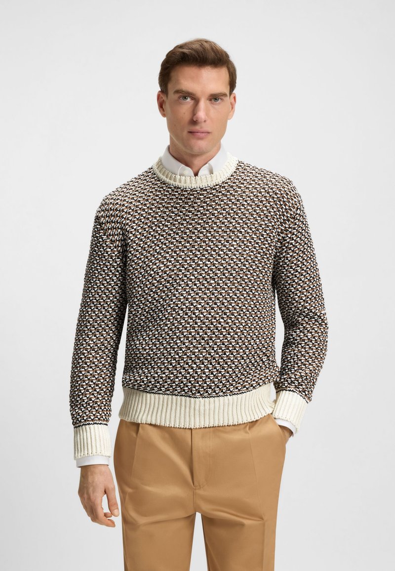 Jersey de punto en tonos marrón y crema con un patrón texturizado. Cuenta con un cuello redondo acanalado y puños, combinado con pantalones beige.