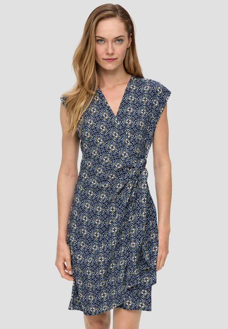 Marineblauwe wikkeljurk met korte capmouwen, voorzien van een geometrisch bloemenpatroon en een strik in de taille, gemaakt van lichte stof.