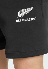 Sort shorts lavet af bomuld, med et hvidt bregne-logo og "ALL BLACKS" tekst på venstre side. Glat tekstur, almindelig pasform.