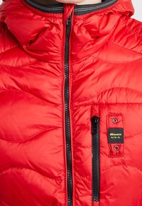 Červená prošívaná bunda s černým předním zipem, malou zipovou náprsní kapsou, označením "Blauer U.S.A." a vycpaným vysokým límcem.