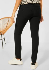 Black fitted pants with a smooth texture, featuring back pockets and a mid-rise design. Complemented by white sneakers.