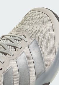 Αθλητικό παπούτσι ανοιχτού γκρι με υφασμένο πλέγμα στο επάνω μέρος, διαθέτει τρεις μεταλλικές γκρι ρίγες, επίπεδα κορδόνια και ενισχυμένη μύτη.