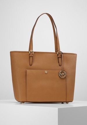 Sac fourre-tout en cuir marron avec double poignée, poche avant et breloque ronde métallique avec logo MK suspendue à une des poignées.