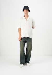 Kortærmet, struktureret cremefarvet skjorte, mørkegrønne vide jeans, hvide sneakers og en sort bøttehat. Enkel og afslappet outfitdesign.