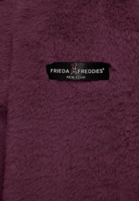 Pluszowy materiał w głębokim burgundzie o miękkiej teksturze. Zawiera metkę z napisem "FRIEDA FREDDIES NEW YORK" w czerni z srebrnym napisem.