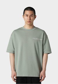 Kortærmet, oversized t-shirt i lysegrøn bomuld med rund hals og tryk på venstre bryst med stiliseret tekst. Glat tekstur.
