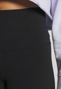 Gros plan d'une personne portant un legging noir taille haute et un haut à manches longues lavande clair laissant le ventre découvert.