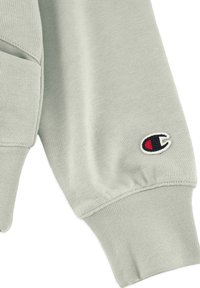 Manga de sudadera verde claro hecha de tela suave, con un puño acanalado y un pequeño logo bordado en negro, rojo y blanco.