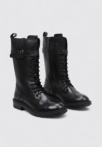 Black leather knee-high boots with a lace-up front, side zipper, buckle accent, and flat sole. Smooth finish with a rounded toe design.