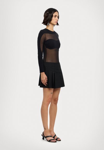 Top nero a maniche lunghe con sezioni trasparenti, abbinato a una mini gonna plissettata nera. Le calzature presentano sandali neri con cinturini.