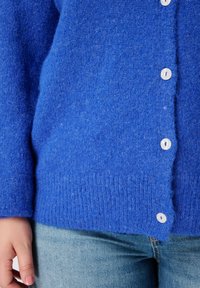 Blauwe wollen cardigan met een zachte textuur, voorzien van witte knopen en een geribbelde zoom. De stof heeft een licht pluizige uitstraling.