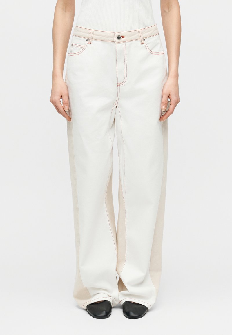 Valkoiset leveälahkeiset housut, joissa on kontrastiväriset beigeet sivupaneelit ja näkyvä punainen ompelu. Housuissa on perinteinen nappi- ja vetoketjusulku.