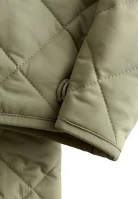 Quilted outerwear in muted olive green, featuring diamond stitching, a smooth texture, and a rolled cuff detail for added functionality.
