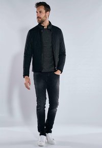 Black quilted jacket with a stand collar over a textured dark gray sweater, paired with dark jeans and white sneakers.
