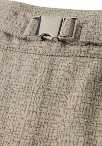 Tela texturizada beige con un patrón sutil, que presenta un detalle de hebilla de metal plateado en la cintura. Diseño ajustado con líneas limpias.