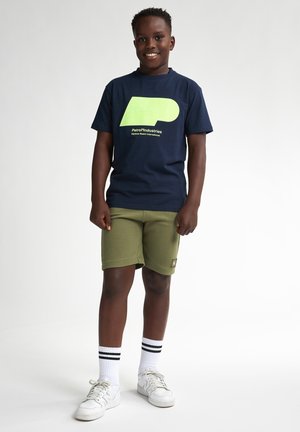 Tricou bleu cu mânecă scurtă, având un grafic verde, asociat cu pantaloni scurți de culoare verde măslin și adidași albi cu dungi negre pe șosete.