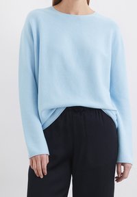 Pull bleu clair texturé avec un col rond et des manches longues, assorti à un pantalon noir ample.