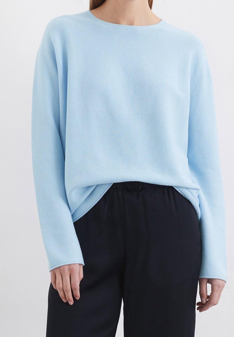 Pull bleu clair texturé avec un col rond et des manches longues, assorti à un pantalon noir ample.