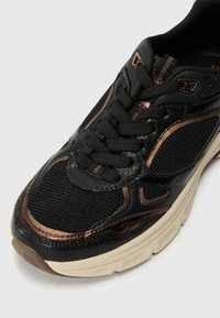 Scarpa atletica nera con materiali in rete e sintetici, caratterizzata da accenti bronzei, finitura testurizzata e una suola spessa e ammortizzata.
