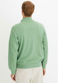 Felpa verde con collo alto, maniche lunghe e vestibilità comoda. Realizzata in tessuto morbido, con polsini e orlo a costine.