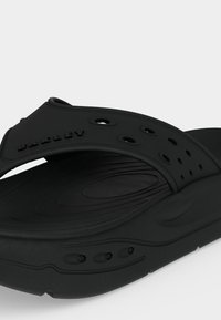 Μαύρο ανατομικό σανδάλι τύπου slide με διατρητό ρυθμιζόμενο λουράκι και υφασμένο πέλμα σχεδιασμένο για άνεση και αερισμό.