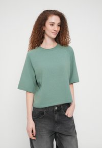 Πράσινο cropped πουλόβερ από πλεκτό με κοντά μανίκια και στρογγυλή λαιμόκοψη. Μαλακή υφή με διακριτικές ριμπ λεπτομέρειες. Φορεμένο με σκούρο γκρι τζιν.