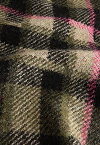 Woolen fabric with a plaid pattern in green, black, beige, and pink. Textured surface with visible fibers and varied weave details.