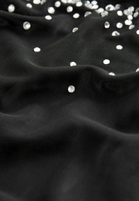Tissu noir texturé avec de petits strass ronds transparents dispersés créant un effet scintillant à la surface.