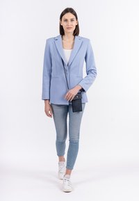Blazer azzurro chiaro con revers, due tasche frontali, abbinato a jeans skinny di lavaggio chiaro e sneakers bianche. Accento di borsa a tracolla nera.