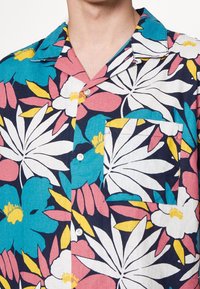 Short-sleeve shirt featuring a floral pattern in turquoise, pink, white, and yellow on a dark navy background, with a chest pocket and buttons.
