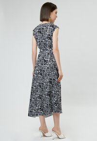Vestido sin mangas de patrón en blanco y negro con cintura ajustada y falda midi fluida. Tejido suave con un acento de print geométrico.