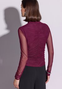 Bordowa bluzka z marszczeniami, dopasowanym fasonem i przezroczystymi długimi rękawami. Gładka faktura, wysoki dekolt i subtelny połysk.