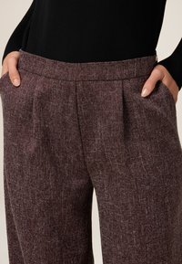 Bordowe, dopasowane spodnie wykonane z teksturowanej tkaniny, z zakładkami z przodu i bocznymi kieszeniami, zestawione z dopasowanym czarnym topem.