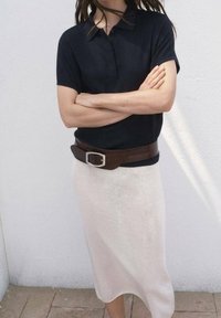 Czarna koszulka polo z krótkim rękawem i kołnierzykiem, w zestawieniu z beżową spódnicą do kolan oraz brązowym paskiem z srebrną klamrą.