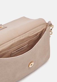 Krémová semišová kabelka se zlatými kovovými prvky, s horním klopným zavíráním, magnetickým uzávěrem a vnitřní kapsou s označením.