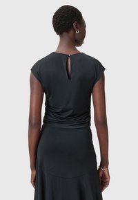 Schwarzes Kleid mit tailliertem Oberteil, kurzen Ärmeln und einem Ausschnitt im Rücken. Weicher Stoff und fließender Rock mit einem mehrlagigen Look.