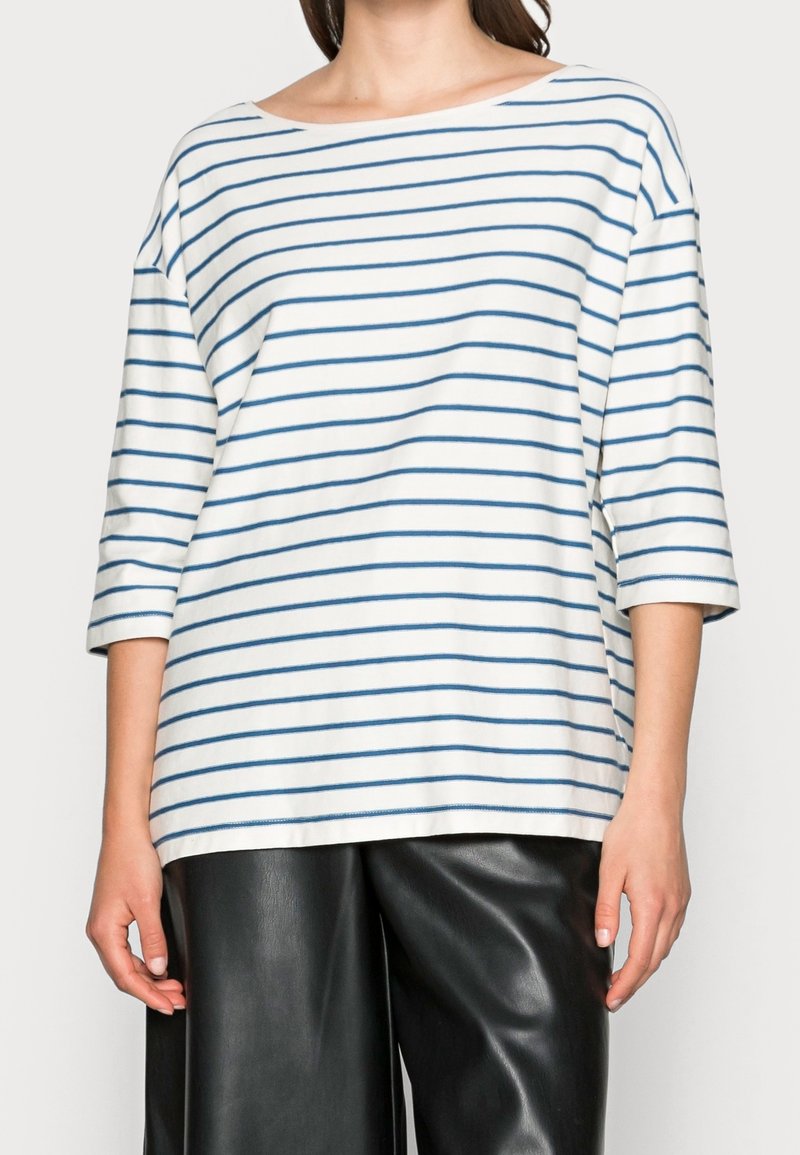 Vit och blå randig skjorta med bred halsringning, trekvartslånga ärmar och lös passform. Bärs med svarta, höga fusk-läderbyxor.