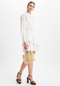 Weißes Kleid mit Rüschensaum, bedruckt mit hellblauen Blumen, gestuftes Design, kombiniert mit einer kleinen geflochtenen Tasche und braunen Plateau-Heels.