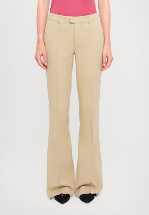 Pantalons évasés beiges avec une texture lisse, poches avant et fermeture à un bouton, associés à des escarpins noirs à bout pointu.